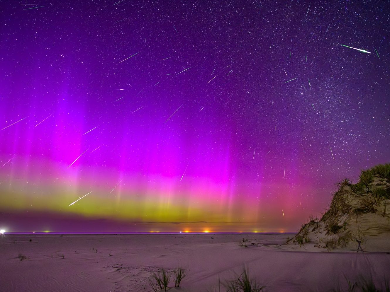 An aurora with meteor streaks over a beach